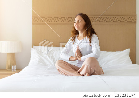 Middle aged caucasian woman meditating on bed at home, practicing mindfulness 136235174