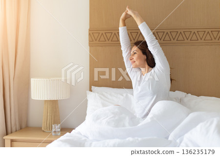 Caucasian middle aged woman stretching arms while sitting in bed 136235179