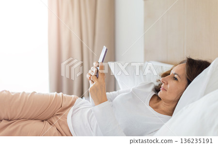 Adult caucasian woman lying on bed at home using smartphone 136235191