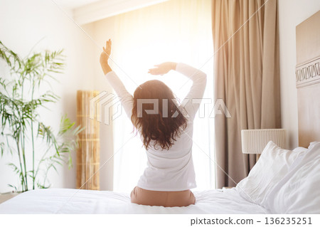 Adult caucasian woman stretching arms while sitting on bed at home Adult caucasian woman stretching arms while sitting on bed at home 136235251