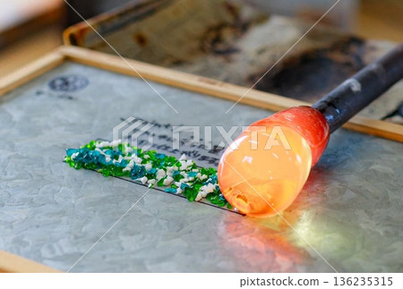 這是使用熔融玻璃和彩色玻璃進行玻璃吹製體驗的場景。 這是使用熔融玻璃和彩色玻璃進行玻璃吹製體驗的場景。 136235315