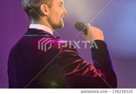 Back view showman singer with microphone on stage in spotlight, velvet suit Back view showman singer with microphone on stage in spotlight, velvet suit 136236520