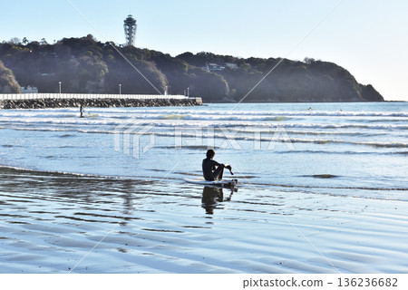 A surfer resting on the shore of Katase Beach, with a view of Enoshima Lighthouse A surfer resting on the shore of Katase Beach, with a view of Enoshima Lighthouse 136236682
