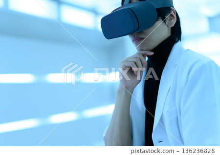 A Japanese male researcher in a white coat thinking while wearing VR goggles 136236828
