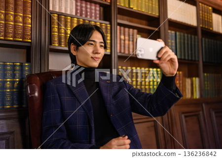 一位穿著夾克的年輕男子正在書房使用智慧型手機。 一位穿著夾克的年輕男子正在書房使用智慧型手機。 136236842