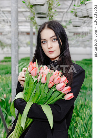 Young woman standing in large greenhouse and holding a blooming tulips in her hands 136238552