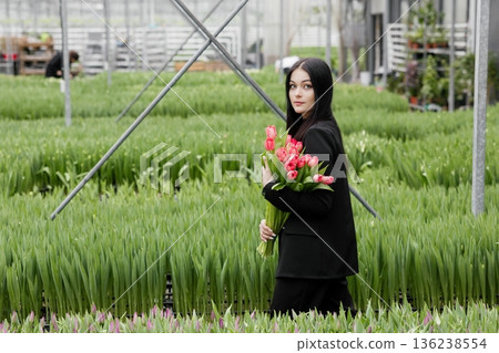 Young woman standing in large greenhouse and holding a blooming tulips in her hands 136238554