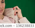 put on a jacket on a green background, chromakey, close-up of a woman with emotions in a beige jacket, red manicure, blue eyes 136238833