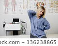 Woman experiencing back and neck pain in clinic 136238865