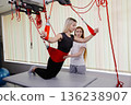 Physiotherapist assisting young woman exercising with suspension training in rehabilitation center 136238907