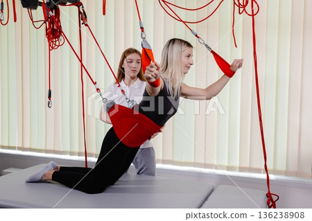 Physiotherapist assisting young woman exercising with suspension training in rehabilitation center Physiotherapist assisting young woman exercising with suspension training in rehabilitation center 136238908