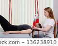 Physiotherapist assisting patient during suspension therapy exercise 136238910