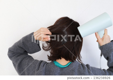 A woman drying her hair with a hair dryer 136238926