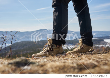 Feet in hiking boots standing on dry grass with mountain landscape. Adventure and active lifestyle concept for travel Feet in hiking boots standing on dry grass with mountain landscape. Adventure and active lifestyle concept for travel 136239664