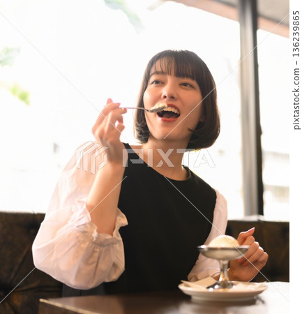 Upper body shot of a young woman enjoying an ice cream in a cafe Upper body shot of a young woman enjoying an ice cream in a cafe 136239865