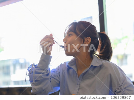 Young man in profile eating dessert with a spoon in a cafe Young man in profile eating dessert with a spoon in a cafe 136239867