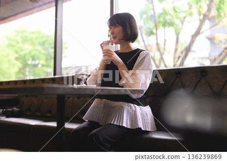 年輕女子在咖啡館的窗邊喝飲料。 年輕女子在咖啡館的窗邊喝飲料。 136239869