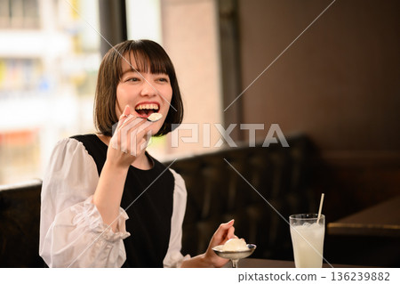 Smiling young woman eating ice cream in a cafe 136239882