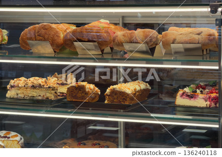 Various delectable fresh baked goods, from sweet fruit cakes and tarts to savory sandwiches, carefully showcased and brightly illuminated in a modern cafe display cabinet Various delectable fresh baked goods, from sweet fruit cakes and tarts to savory sandwiches, carefully showcased and brightly illuminated in a modern cafe display cabinet 136240118