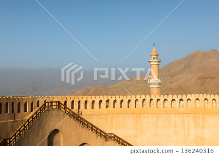 Nizwa Fort walls and minatret of Al Qalaa Mosque in afternoon light in Oman Nizwa Fort walls and minatret of Al Qalaa Mosque in afternoon light in Oman 136240316