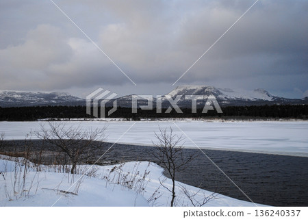 Snow-covered fields and a winding river with distant mountains on the Kuril Islands under an overcast winter sky. Snow-covered fields and a winding river with distant mountains on the Kuril Islands under an overcast winter sky. 136240337