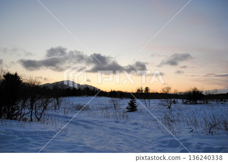 Snowy road and field leading to mountains on the Kuril Islands at sunset, showing volcanic peaks, coastal expanse and quiet winter light. Snowy road and field leading to mountains on the Kuril Islands at sunset, showing volcanic peaks, coastal expanse and quiet winter light. 136240338