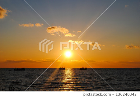 The photograph showcases a stunning view of a sea bay on the Kuril Islands at sunset, with vessels gently resting on the water. 136240342