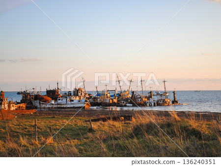 The photograph captures a striking view of a sea bay and a haunting ship graveyard on the Kuril Islands at sunset. The photograph captures a striking view of a sea bay and a haunting ship graveyard on the Kuril Islands at sunset. 136240351