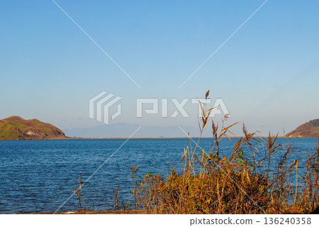 The photograph captures a breathtaking view of a sea bay and autumn forest on the Kuril Islands during sunset on a sunny day. The photograph captures a breathtaking view of a sea bay and autumn forest on the Kuril Islands during sunset on a sunny day. 136240358