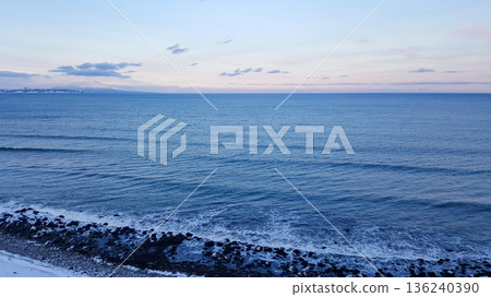 A view showcases the snowy Pacific coastline of the Kuril Islands, featuring striking black volcanic sand and a distant volcano. A view showcases the snowy Pacific coastline of the Kuril Islands, featuring striking black volcanic sand and a distant volcano. 136240390