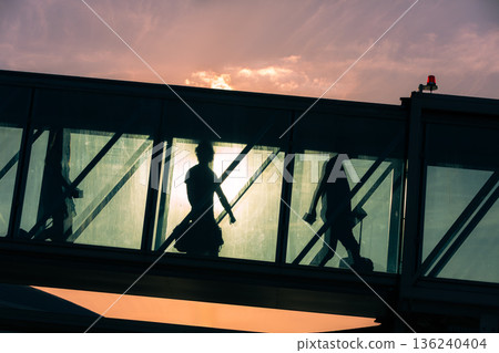 Passengers walking through boarding bridge to airplane at airport Passengers walking through boarding bridge to airplane at airport 136240404