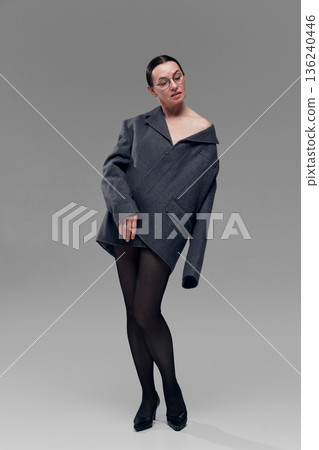 Woman wearing oversized blazer styled off shoulder in minimalist studio. 136240446