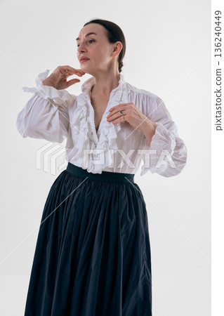 Classic woman in white ruffled blouse posing in studio portrait with soft confidence. Classic woman in white ruffled blouse posing in studio portrait with soft confidence. 136240449