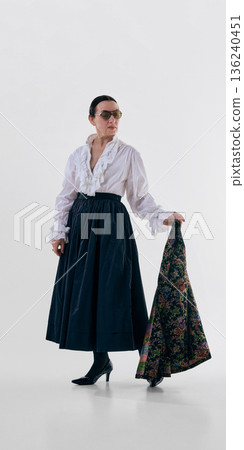 Elegant mature woman holding floral jacket with thoughtful emotion. 136240451