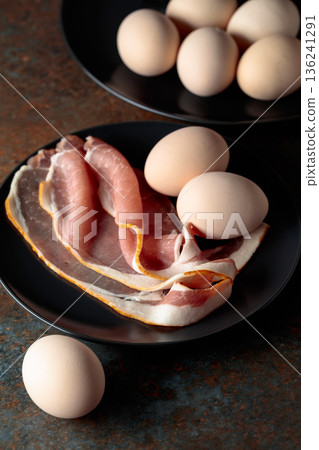 Smoked pork bacon with eggs on a black plate. Smoked pork bacon with eggs on a black plate. 136241291