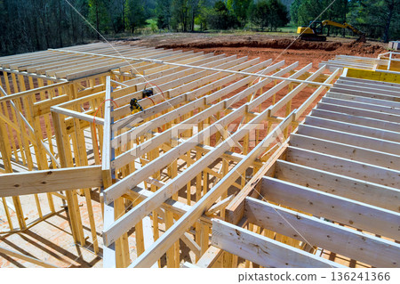Workers are framing roofing joist building with wooden beams on construction site an excavator nearby. 136241366