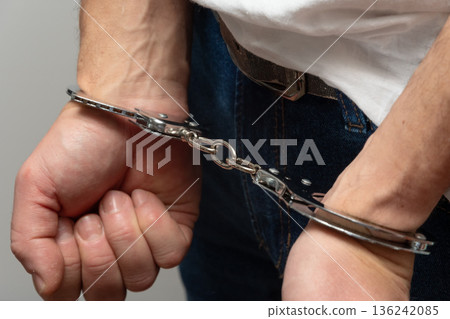 Man clenching fists while wearing handcuffs. 136242085