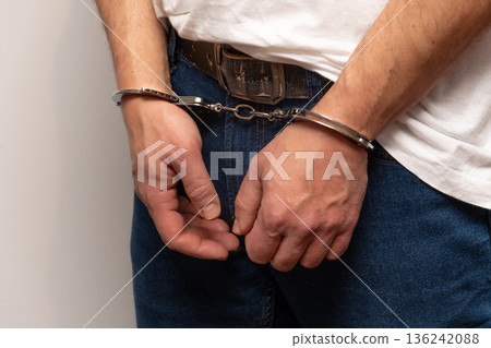 Male hands restrained with metal handcuffs in front. 136242088