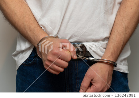 Man in handcuffs stands on neutral background after police detention. Man in handcuffs stands on neutral background after police detention. 136242091