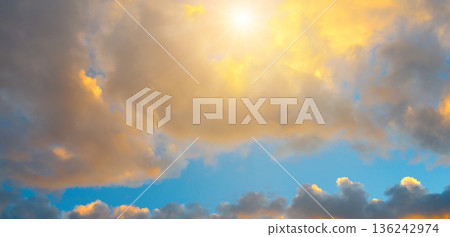 Radiant golden sunrise through dramatic clouds in a blue sky Radiant golden sunrise through dramatic clouds in a blue sky 136242974