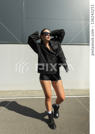 Modern streetwear style portrait of a female model in black outfit with bold attitude. Fashion pretty urban lady with sunglasses 136243251