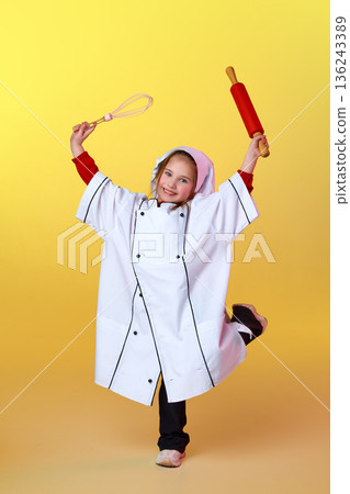Child in chef costume holding baking utensils. Child in chef costume holding baking utensils. 136243389