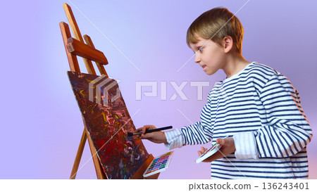Young boy painting abstract artwork on easel. 136243401