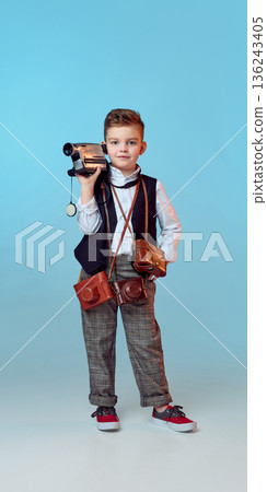 Young boy holding vintage camcorder and looking at camera. 136243405