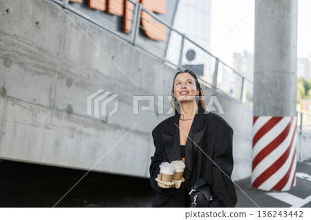 Fashionable girl in oversized blazer and crop top walking outside, holding takeaway coffee and radiating happiness. Fashionable girl in oversized blazer and crop top walking outside, holding takeaway coffee and radiating happiness. 136243442