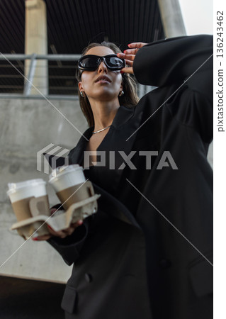 Modern woman with sunglasses holding coffee cups, showcasing minimalistic urban fashion. Modern woman with sunglasses holding coffee cups, showcasing minimalistic urban fashion. 136243462