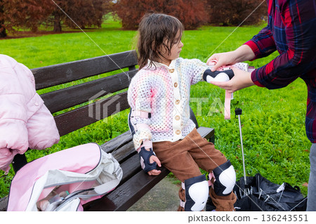 Caucasian young girl preparing for roller skating with protective gear in park Caucasian young girl preparing for roller skating with protective gear in park 136243551