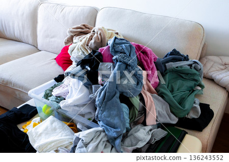 Overflowing laundry pile on sofa with mixed clothing colors 136243552