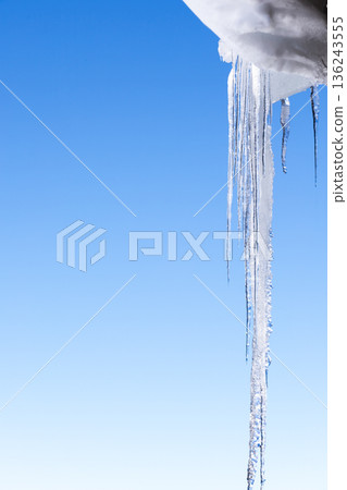 Icicles hanging from snow covered roof against clear blue sky Icicles hanging from snow covered roof against clear blue sky 136243555