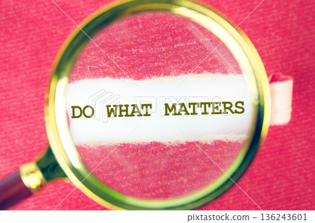 Focusing a magnifying glass on the powerful message do what matters written on white paper. The scene rests on a vibrant red background Focusing a magnifying glass on the powerful message do what matters written on white paper. The scene rests on a vibrant red background 136243601